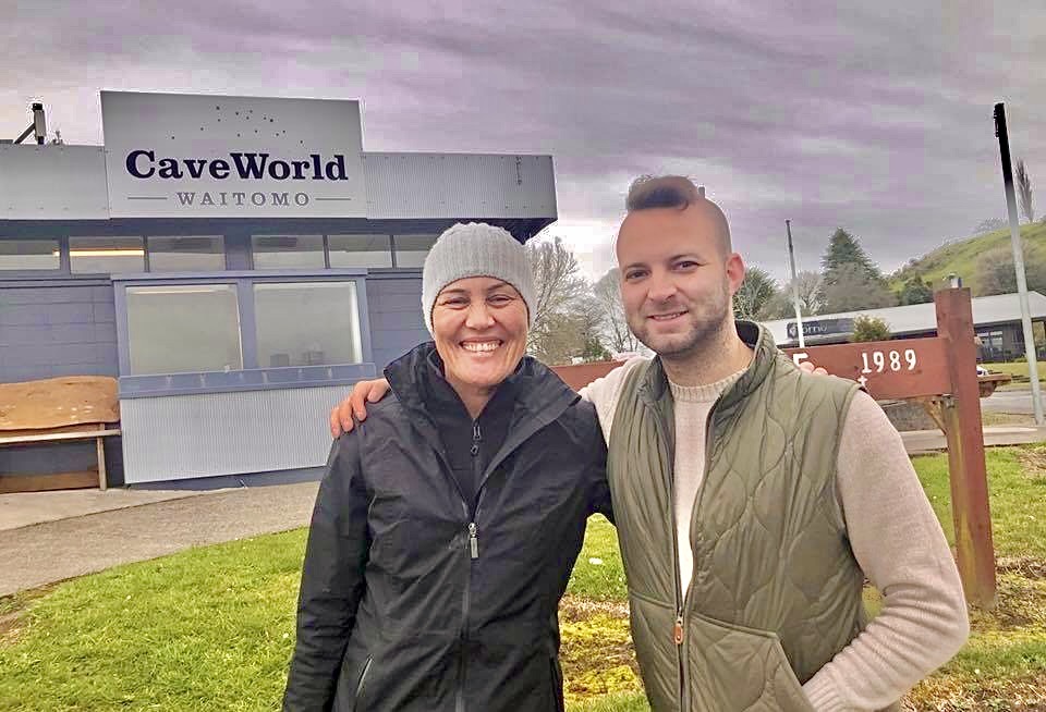 Two people smiling and hugging in front of Cave World Waitomo